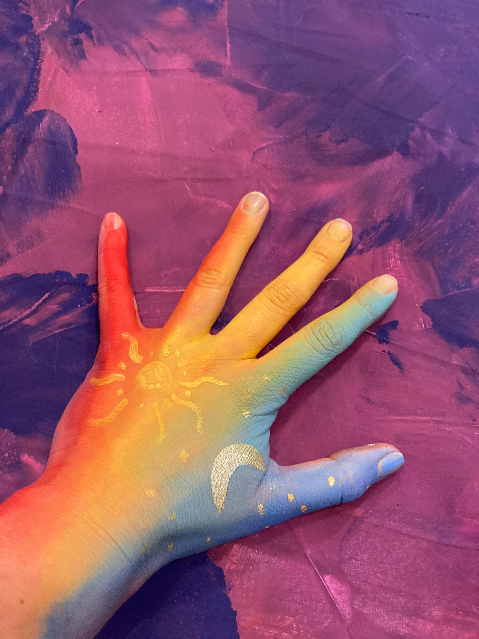 Eine mit bunten Farben und einer Sonne bemalte Hand auf violettem Untergrund
